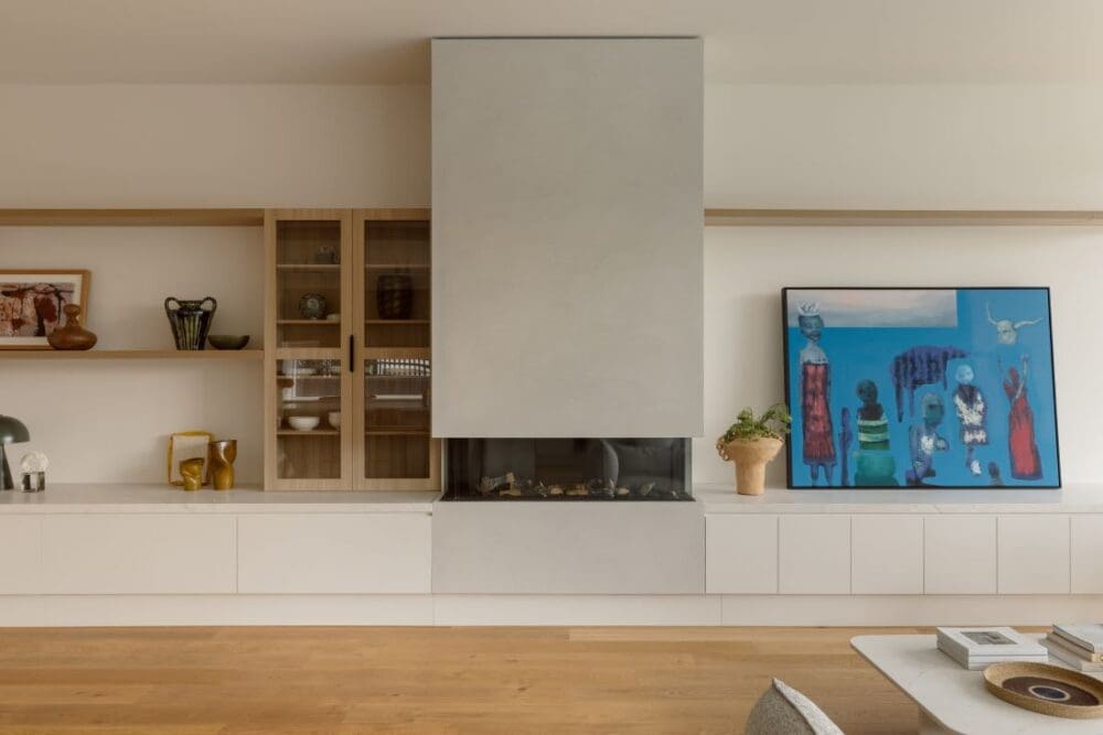 A modern living room featuring a sleek, built-in fireplace, light wood flooring, and a large colorful painting on the wall