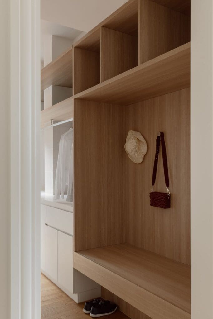 A minimalist entryway mudroom featuring wooden shelving with open cubbies, a bench seat, and space for shoes