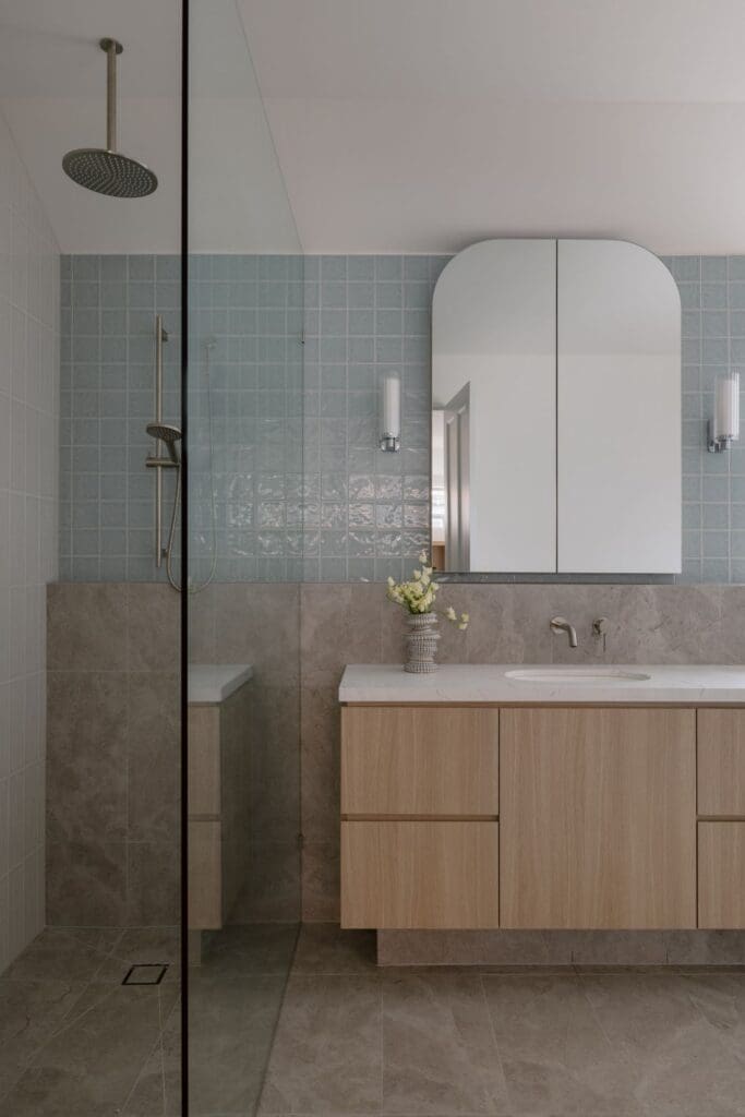 A contemporary bathroom featuring a wooden vanity with a marble countertop, a square blue tiled shower wall, and a stylish mirror above the sink
