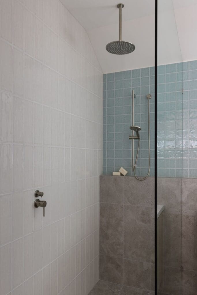 A minimalist shower featuring light grey and blue geometric tiles, a rain showerhead, and a sleek glass partition for a clean, modern look.