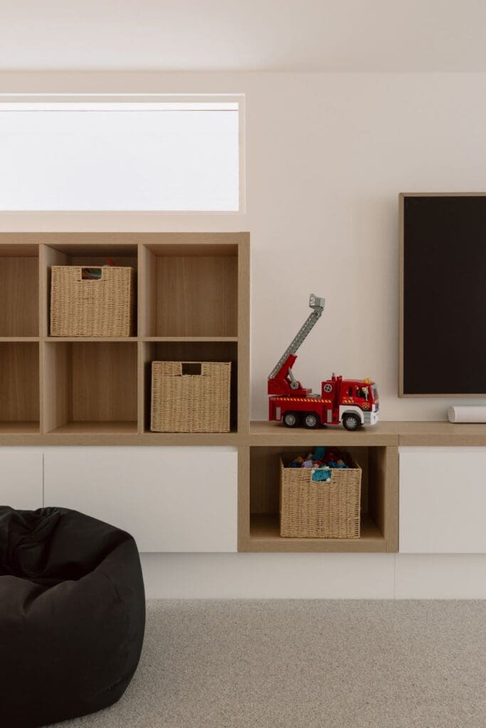A close-up of the storage unit in a kid's playroom featuring woven baskets, a fire truck toy, and a black bean bag chair