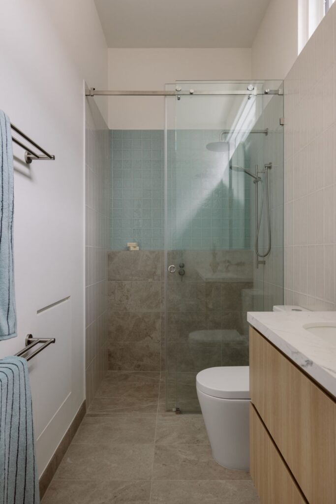 A minimalist bathroom with a glass shower, blue-tiled wall, and wooden vanity