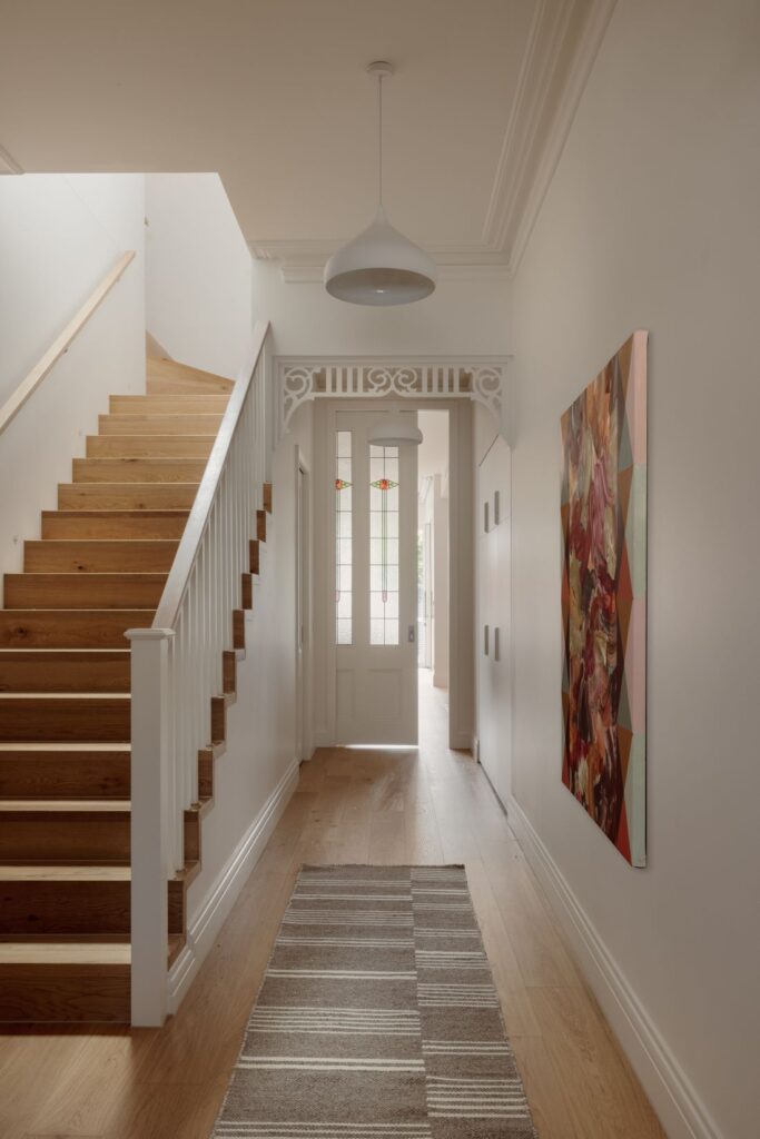 A traditional entryway with wooden stairs, a decorative light fixture, and a vibrant piece of artwork on the wall, leading to the front door