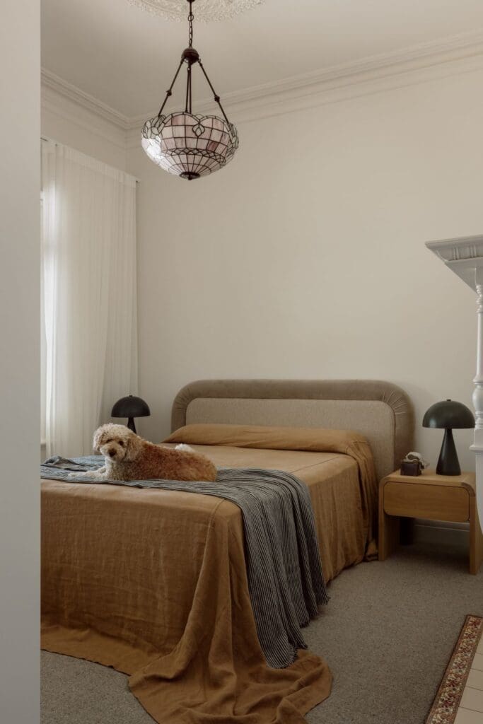 A cosy bedroom featuring soft linens, a modern pendant light, and a dog resting on the bed, creating a warm and inviting atmosphere