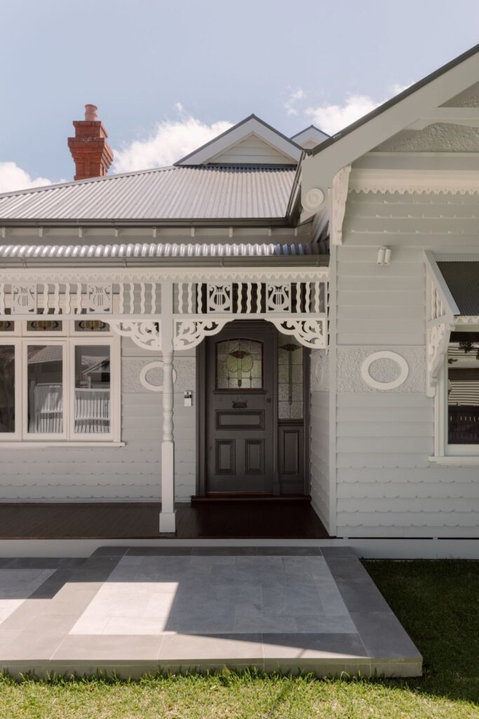 A close-up of the front entrance of a traditional home featuring a dark front door with a stained-glass window, intricate woodwork, and a paved entryway