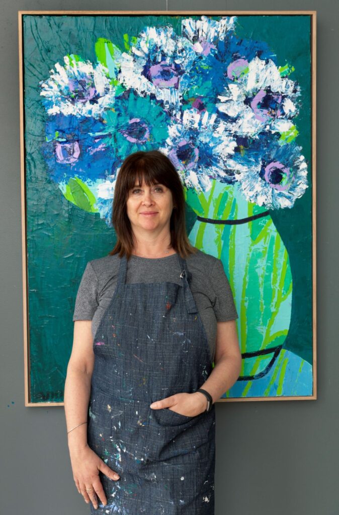 Artist portrait beside large floral artwork