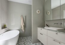 A stylish bathroom featuring a freestanding bathtub, soft green tiles, modern double sconces, and a marble-topped vanity.
