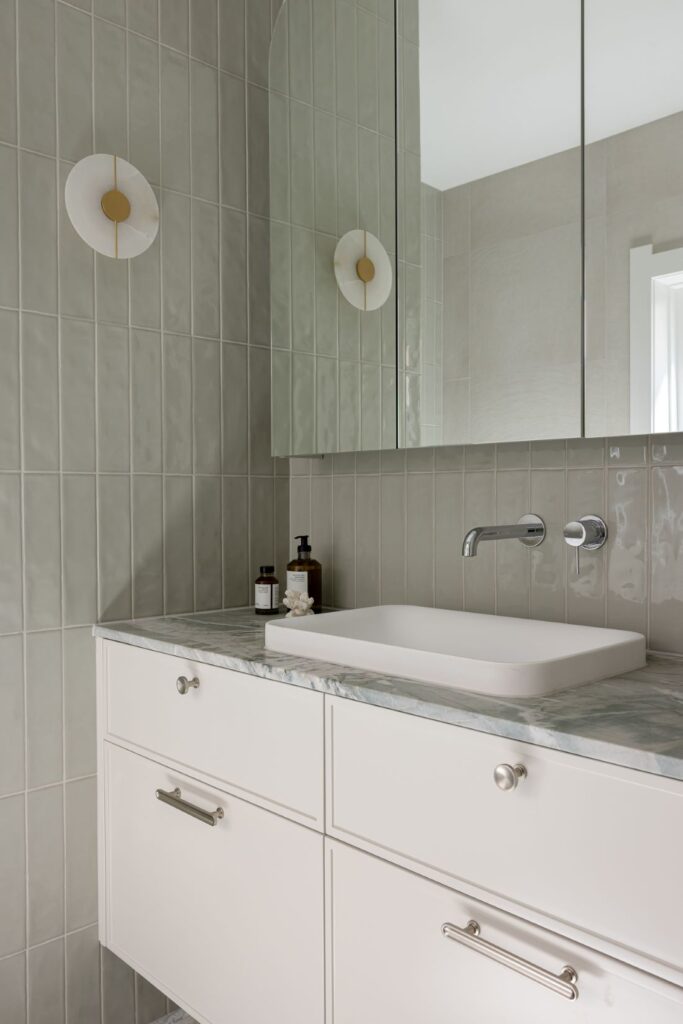 A white bathroom vanity with a marble countertop, sleek faucet, and minimalistic design, complemented by modern wall sconces.