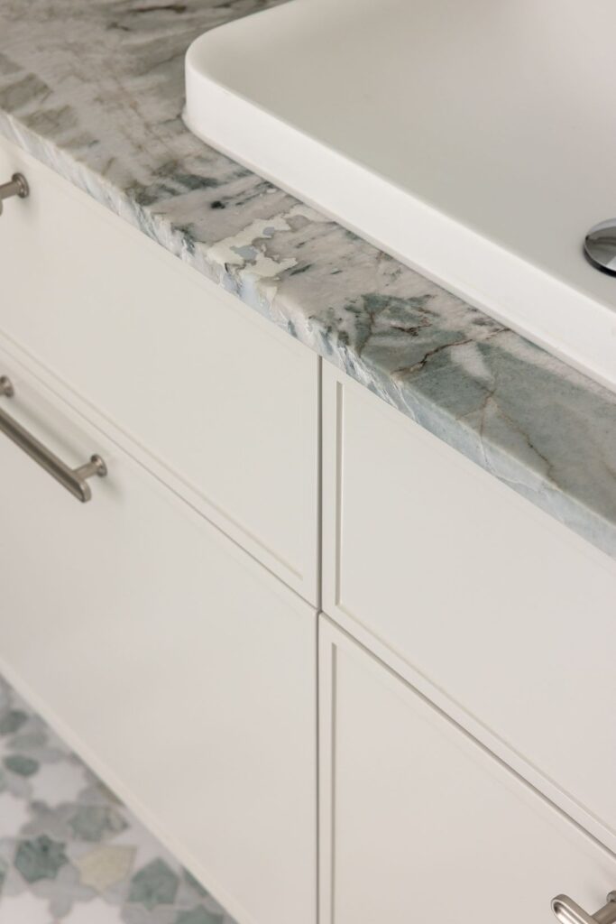 Close-up of a marble vanity countertop with a sleek white basin and modern cabinetry below.