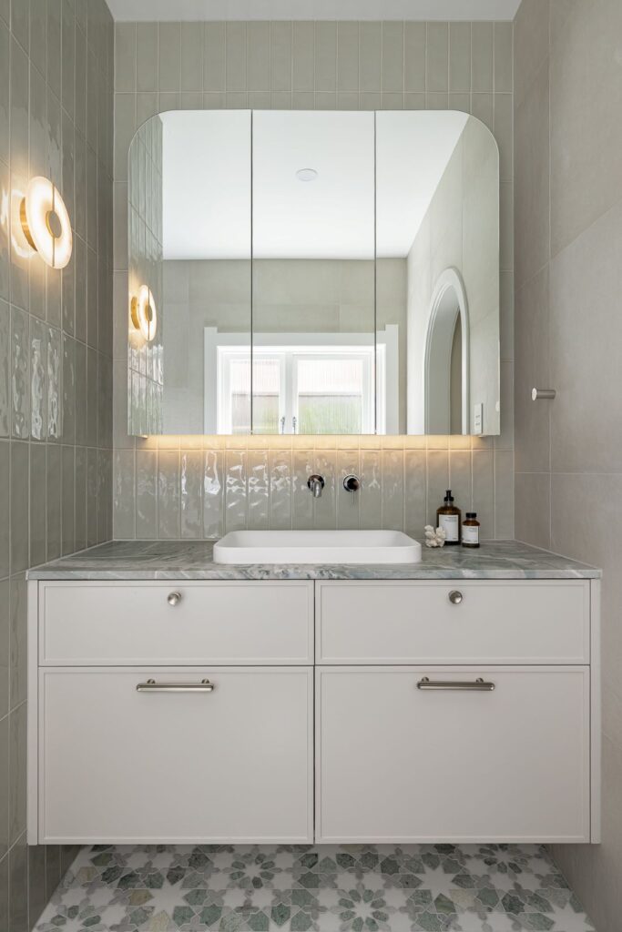 A minimalist bathroom vanity with a marble countertop, sleek mirror, and wall-mounted faucet, complemented by soft green tiles.
