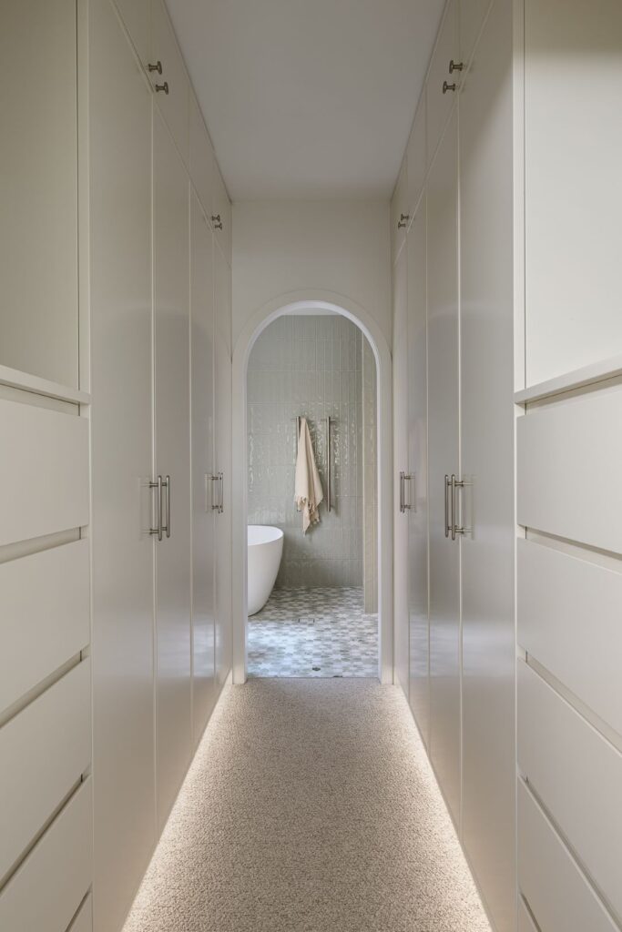A spacious walk-in wardrobe with sleek cabinetry, soft carpet, and ambient lighting, leading into a serene bathroom.