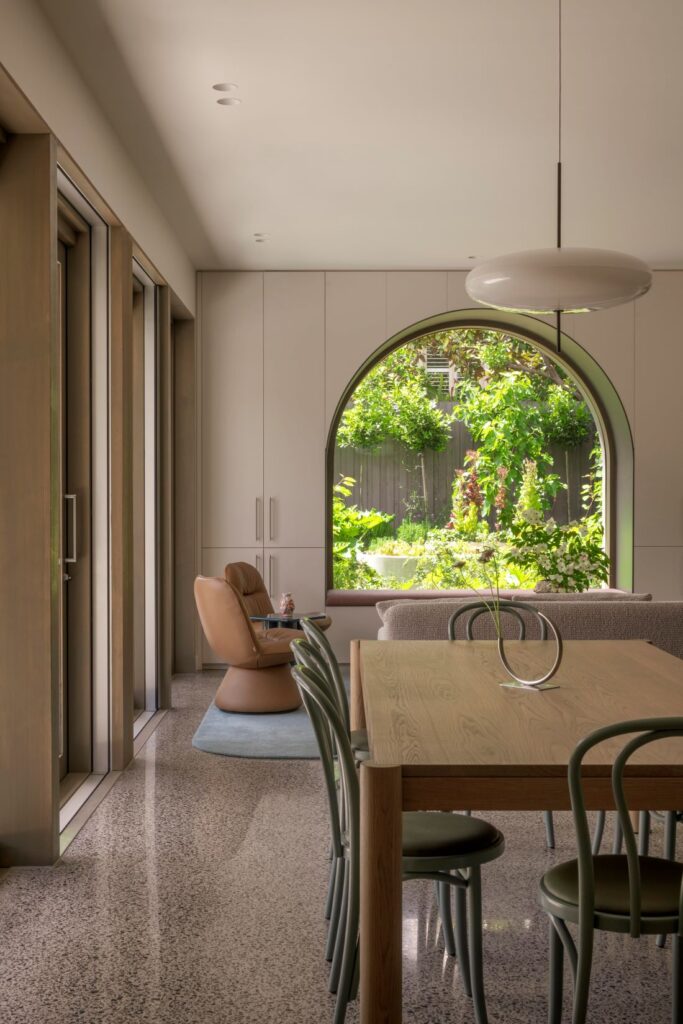 Modern dining space with wooden table and a curved window framing the lush garden outside.