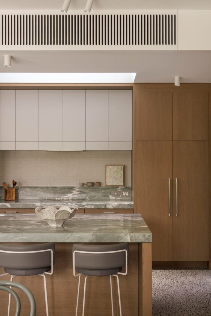 Modern kitchen featuring a marble countertop, natural wood cabinetry, and minimalist bar stools.