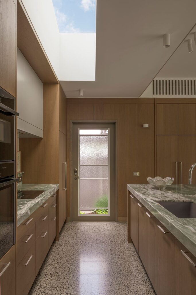 Contemporary kitchen featuring natural wood cabinetry, marble countertops, and a skylight.