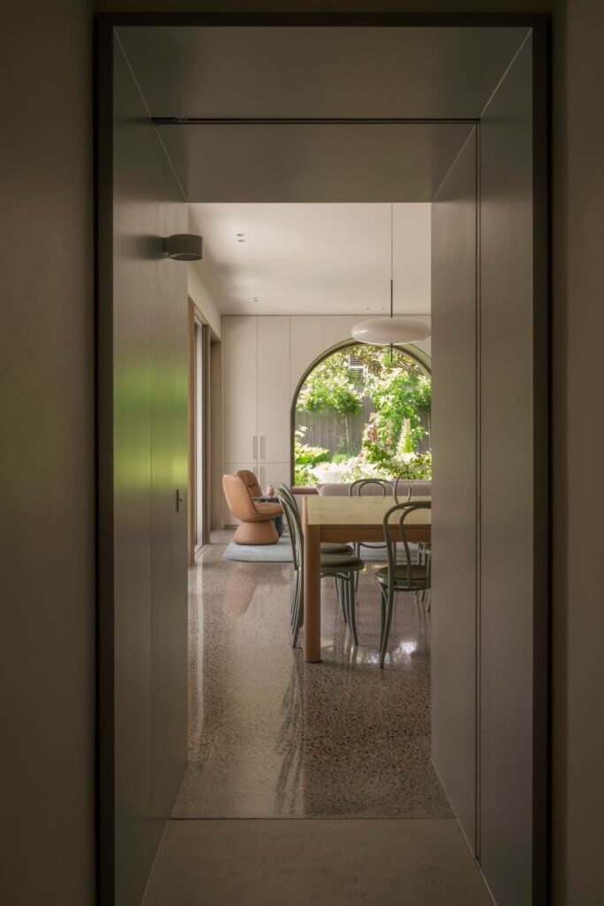 Elegant view of the dining area through a minimalist hallway with terrazzo flooring and natural light.