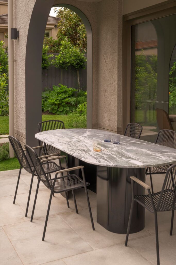 Stylish outdoor dining table with a marble top, surrounded by sleek black chairs, set against a lush garden backdrop.