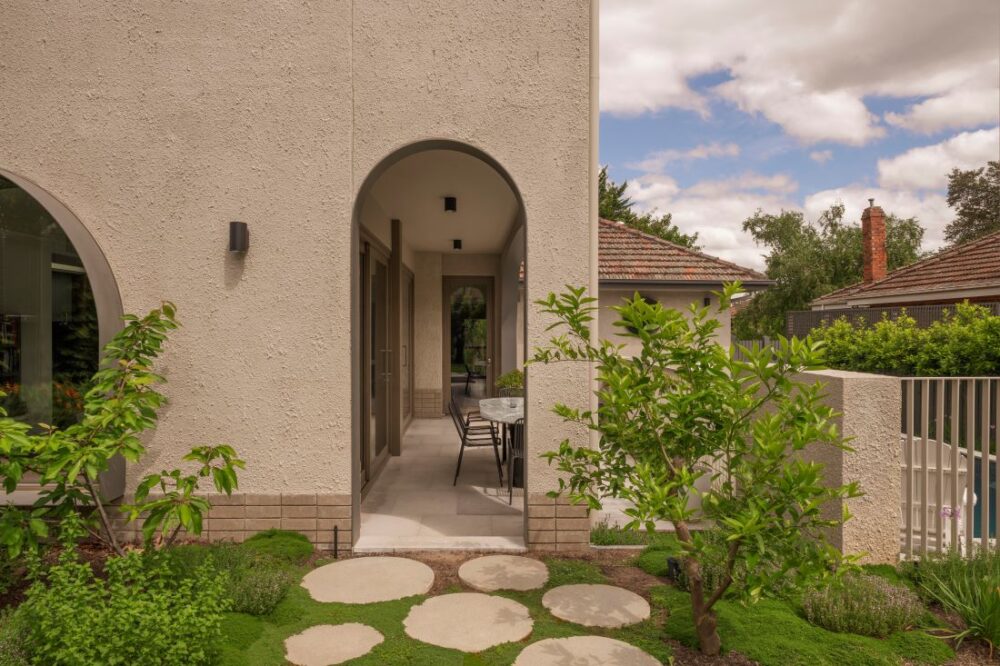 Stone pathway leading to an outdoor dining space with lush greenery and arched openings.