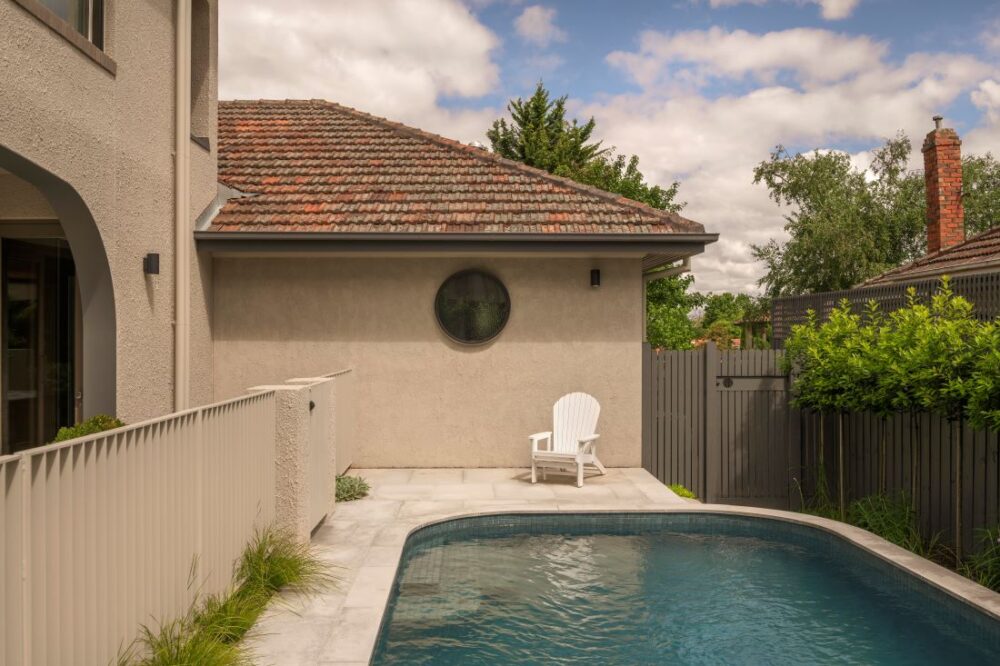 Relaxing poolside area with a white Adirondack chair and a circular window on the wall.