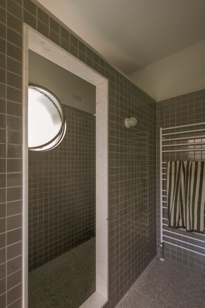 Contemporary shower space featuring grey tiled walls, a circular window, and a towel rail.