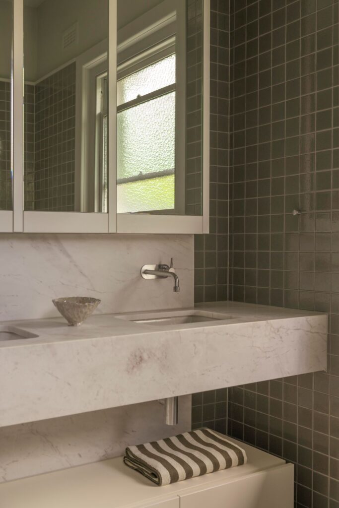 Stylish bathroom vanity with marble sink, sleek mirrors, and textured grey tiles.
