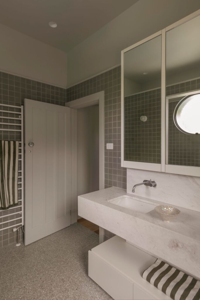 : Clean and modern bathroom with a marble sink, sleek cabinets, and a circular window.