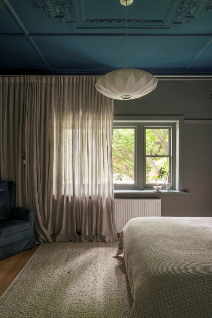 Inviting bedroom with a deep blue ceiling, soft curtains, and natural light filtering through the window.
