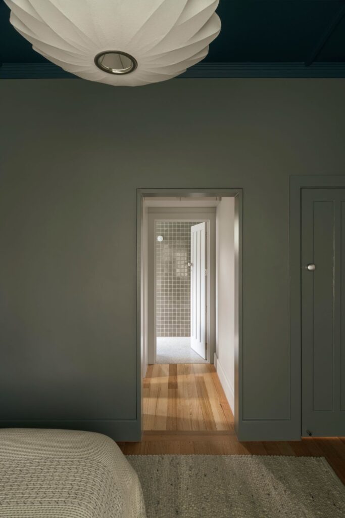 Tranquil bedroom with a deep blue ceiling, natural light, and a view of the bathroom through an open door.