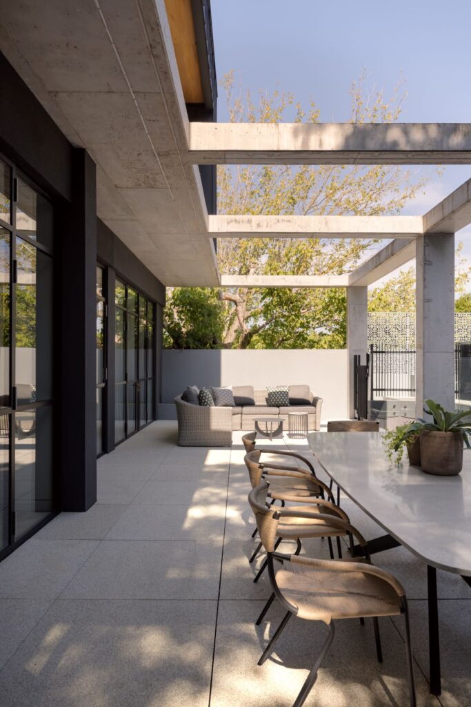 Outdoor alfresco area with modern dining table, comfortable seating, and concrete beams overhead.