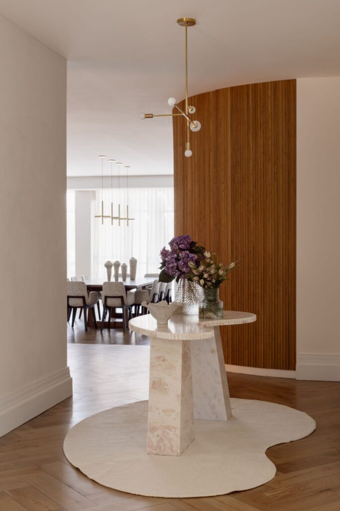 Stylish entrance with a marble pedestal table, floral arrangement, and textured wood partition.