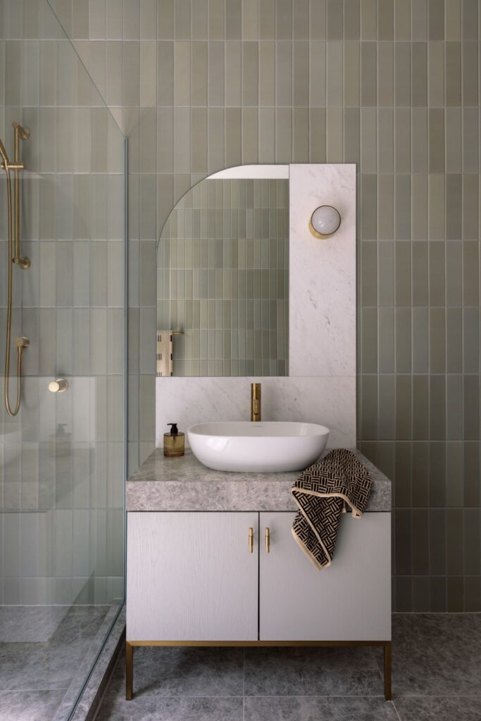 Elegant bathroom with a marble vanity, gold fixtures, and soft green tiles.