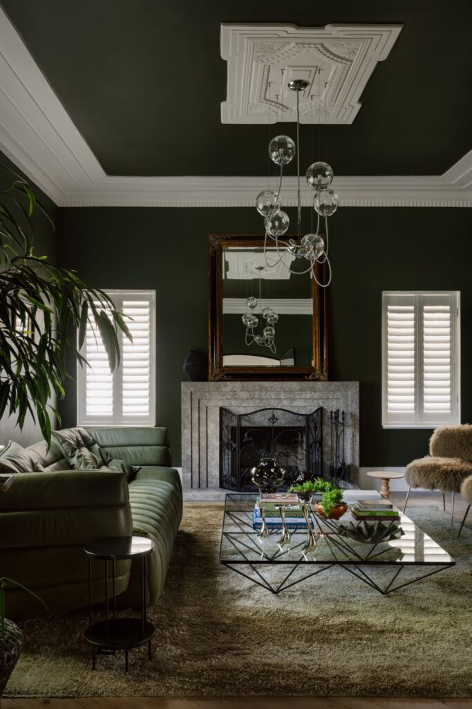 Elegant living room with deep green walls, a marble fireplace, and modern lighting fixtures.