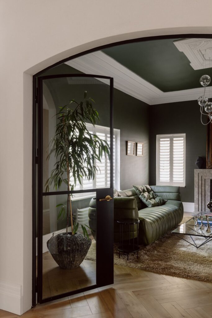 View through a black-framed archway into a living room with deep green walls and sophisticated decor.