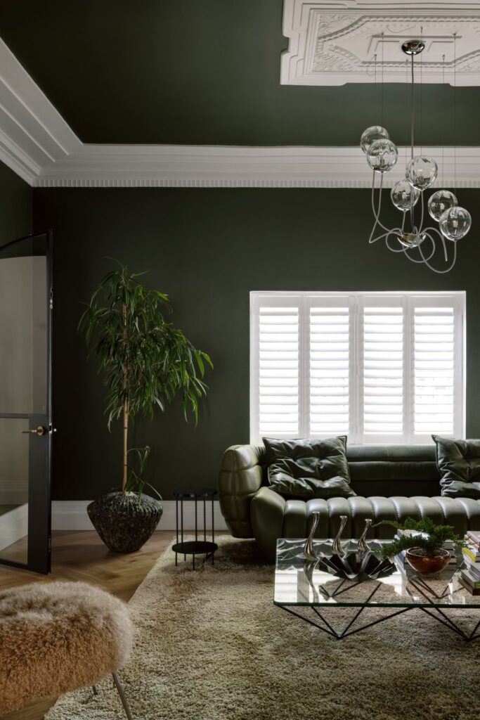 Modern living room with deep green walls, a sculptural sofa, and contemporary lighting fixtures.