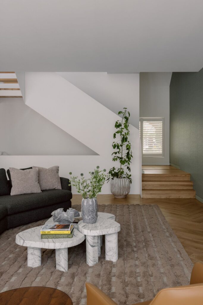 Modern living room featuring marble coffee tables, a plush sofa, and natural wood stairs.