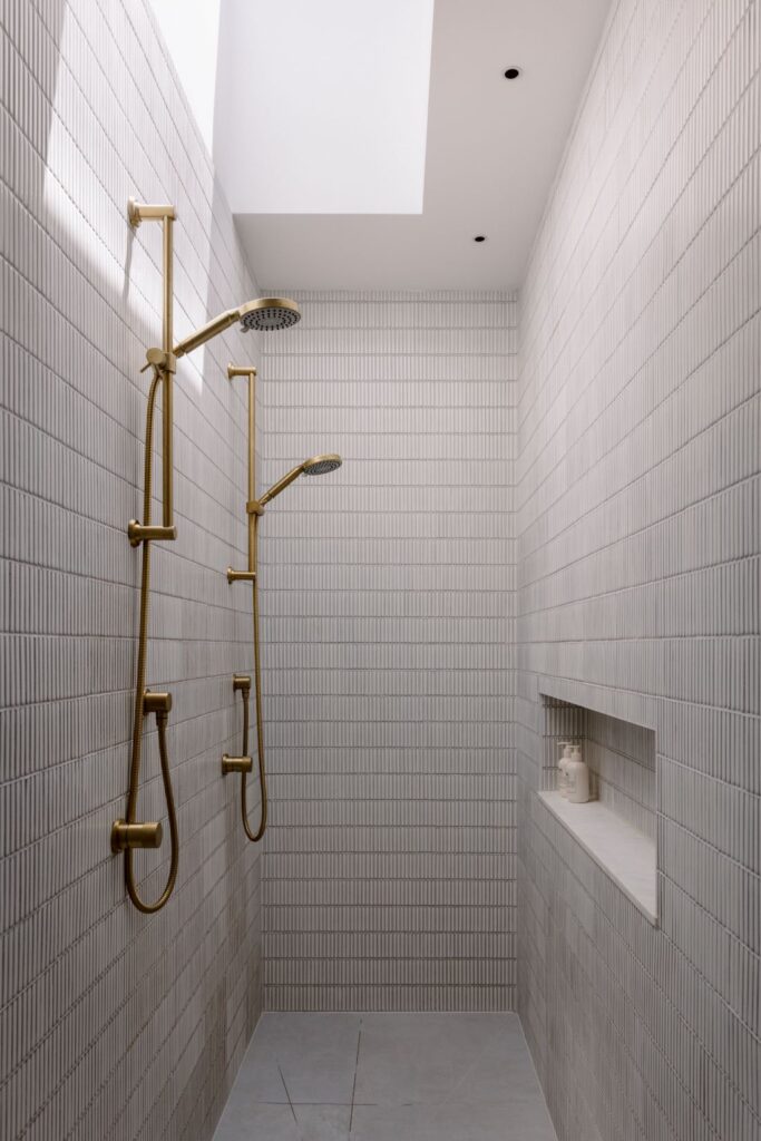 Elegant shower with brass showerheads, textured tiles, and a skylight above.