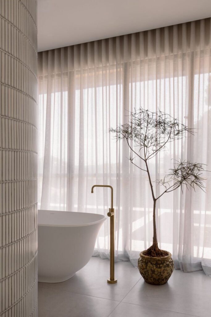 Elegant bathroom with a freestanding tub, brass faucet, and soft light filtering through sheer curtains.