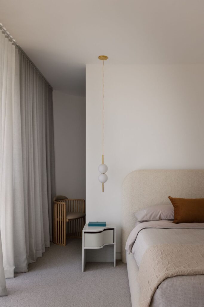 Modern bedroom with a soft upholstered bed, minimalist furniture, and elegant pendant light.