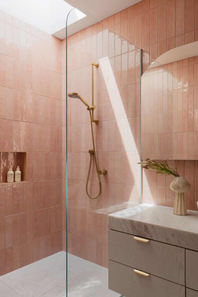 Luxurious shower with soft pink tiles, gold showerhead, and a marble vanity.