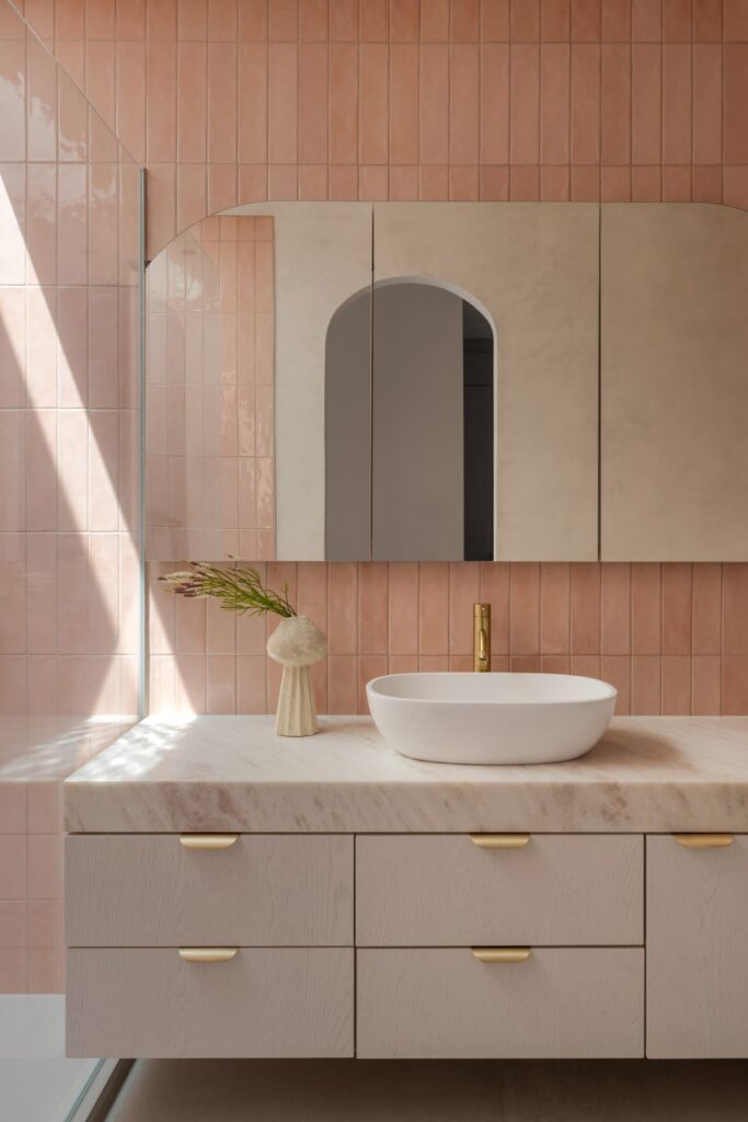Modern bathroom with pink tiles, marble countertop, and brass faucet.