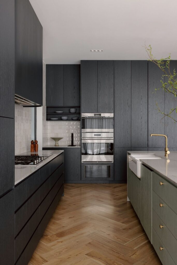 ontemporary kitchen with dark cabinetry, integrated appliances, and sculptural brass tapware.