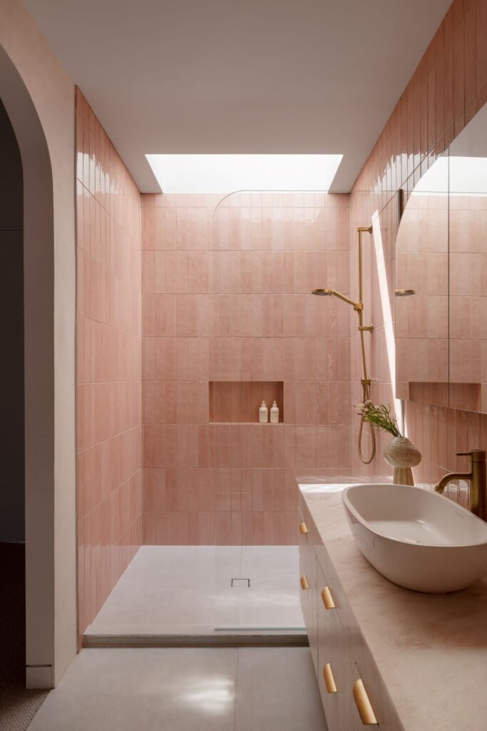 Elegant shower with pink tiles, brass shower fixtures, and a modern marble vanity.