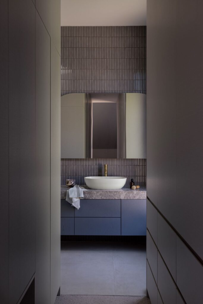 Elegant bathroom with a sculptural sink, textured wall tiles, and sleek cabinetry.