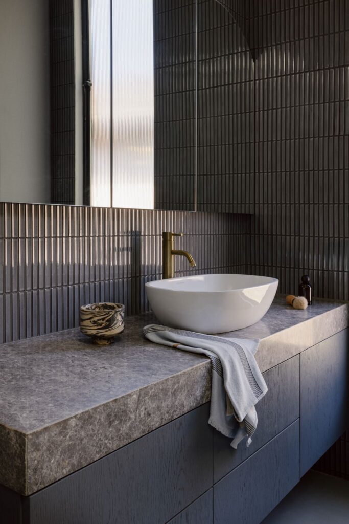 Minimalist bathroom with a sleek countertop, sculptural sink, and brass faucet.