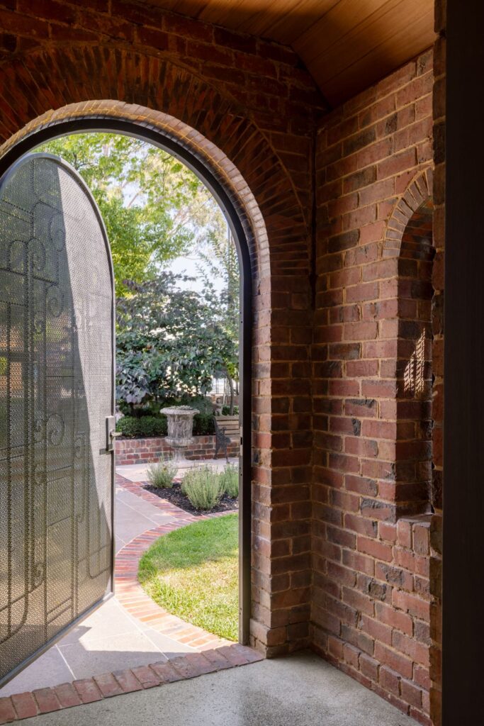 Brick archway and metal gate opening to a manicured garden with a stone fountain.