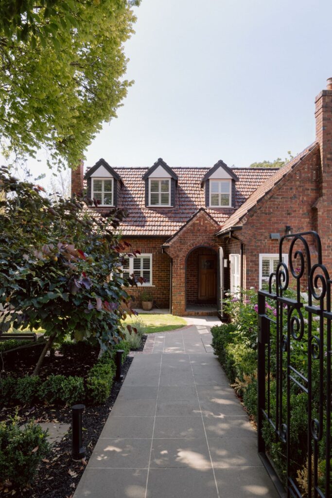 Charming Tudor-style home with a brick facade, welcoming pathway, and vibrant garden.