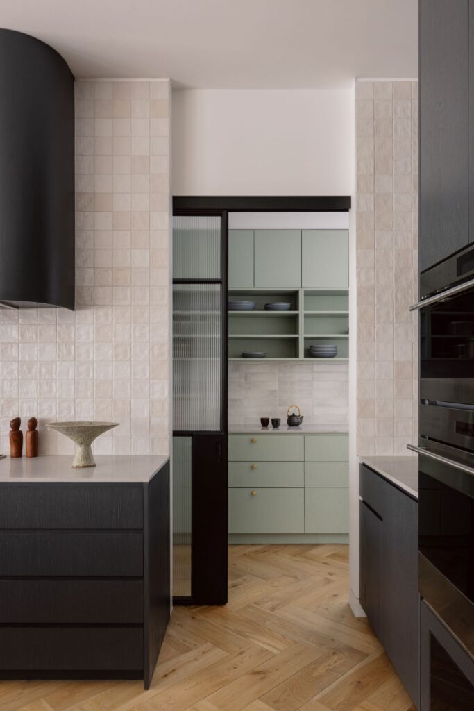 Modern kitchen featuring dark cabinetry, textured tiles, and a green storage area.
