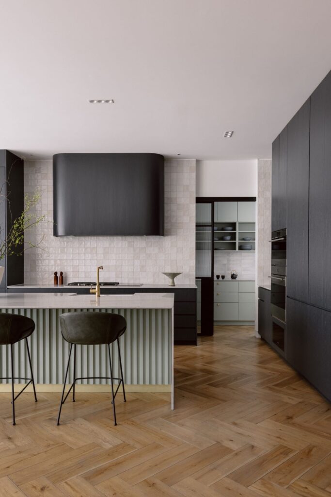 Modern kitchen featuring a sculptural island, dark cabinetry, and a touch of green storage.