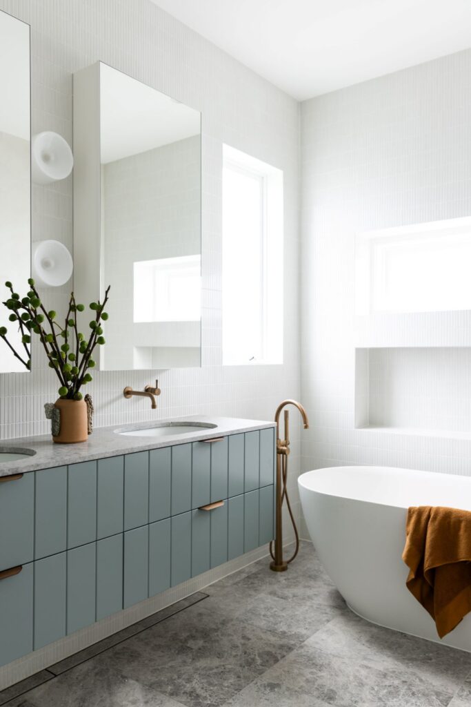 Modern bathroom with blue vanity, freestanding tub, and brass fixtures by Annie Bowen at North Avoca Beach House.