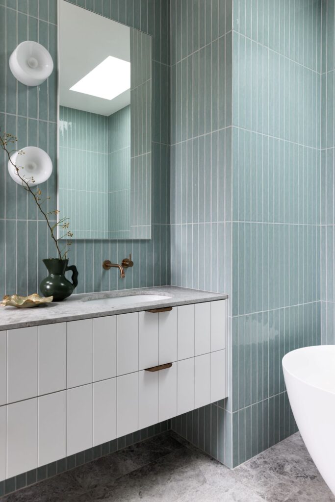 Modern bathroom with blue vertical tiles, white vanity, and freestanding tub by Annie Bowen at North Avoca Beach House.