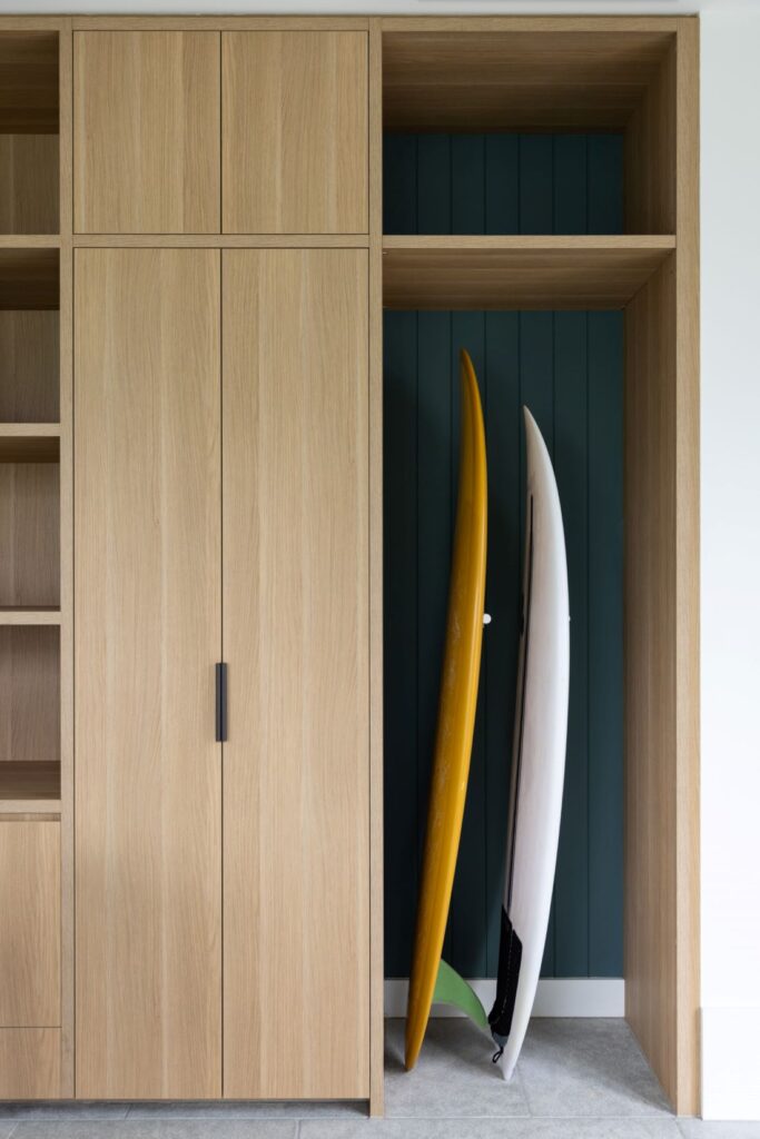 Organized storage area with surfboards, wooden cabinetry, and contrasting wall by Annie Bowen at North Avoca Beach House.